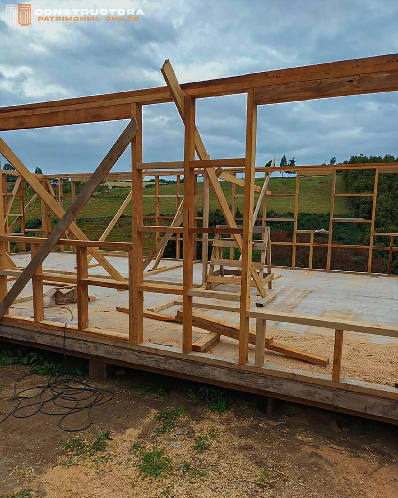Entramado de muros perimetrales en madera sobre la losa, con el campo chilote de fondo